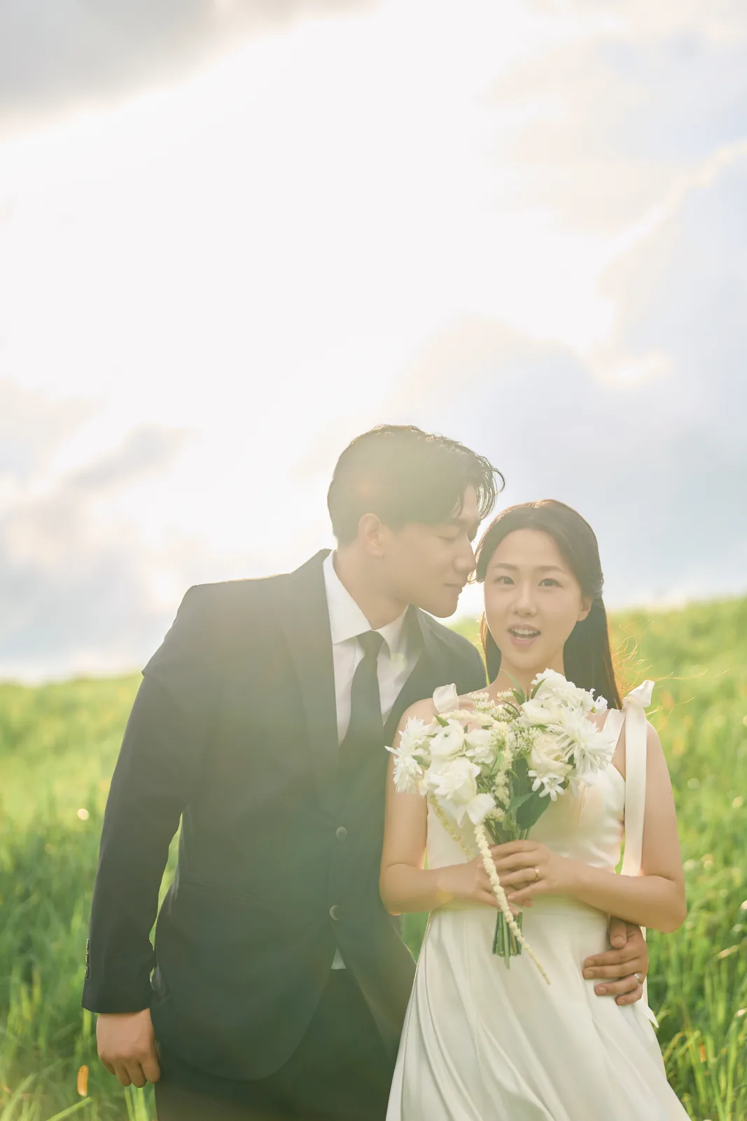 초원에서 부케를 든 정다희의 볼에 홍민의가 입 맞추는 제주 웨딩 스냅